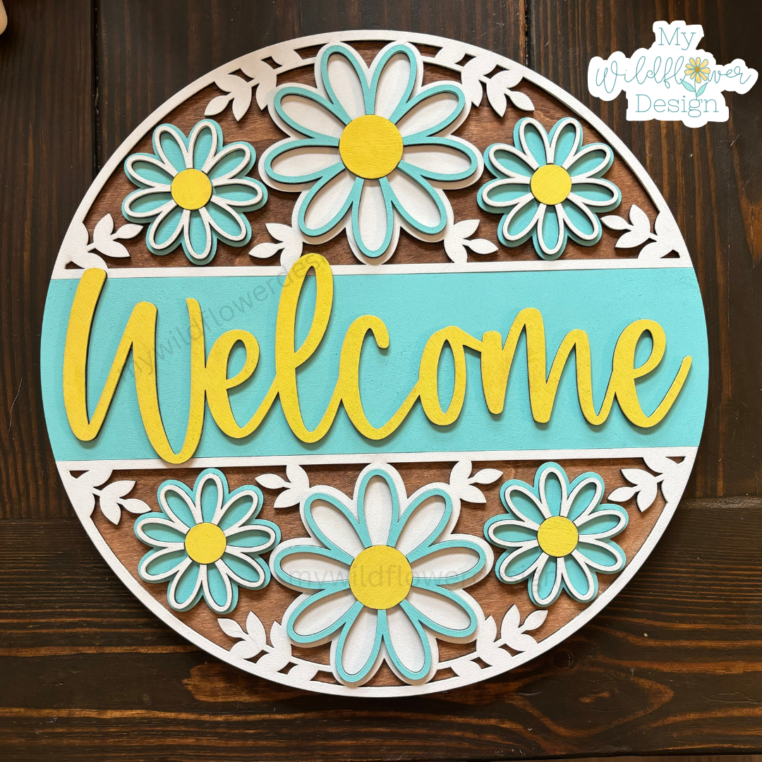 Decorative round sign with flowers and 'Welcome' text on a wooden background