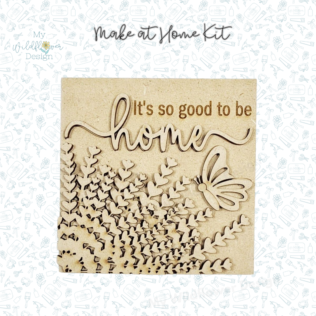 Wooden decorative panel with 'It's so good to be home' text and butterfly design on a light blue patterned background.