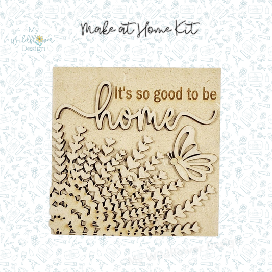 Wooden decorative panel with 'It's so good to be home' text and butterfly design on a light blue patterned background.